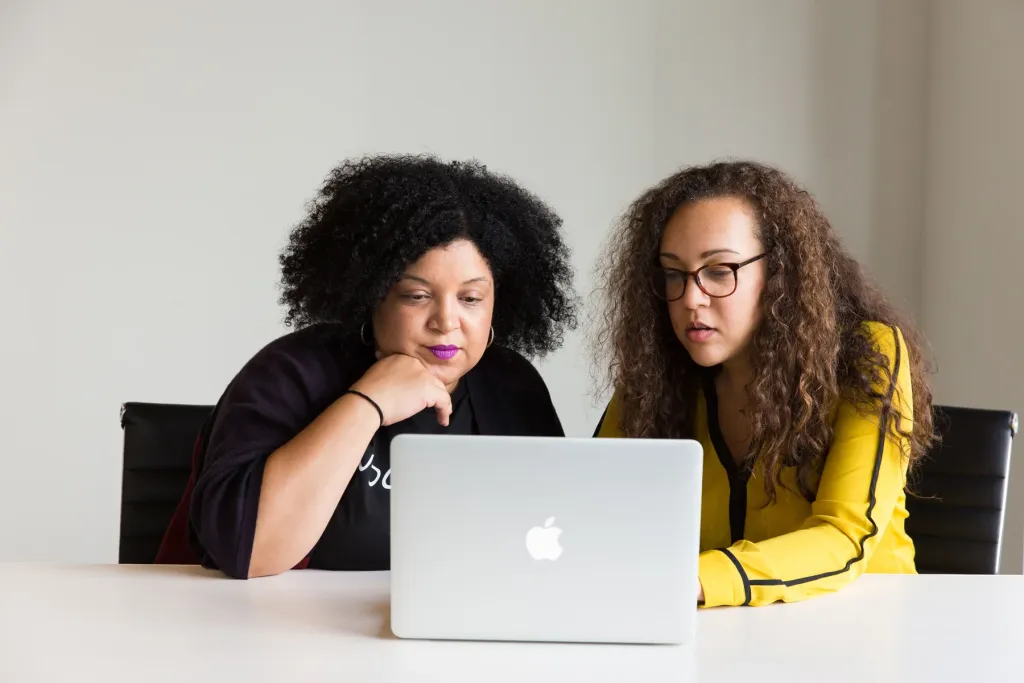 Two women reviewing something on a laptop together, both faces clearly visible