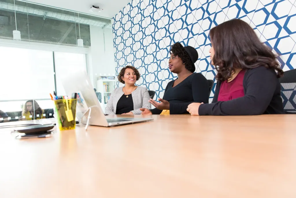 Tr&ecirc;s colegas a discutir o trabalho &agrave; volta de uma mesa com um port&aacute;til aberto