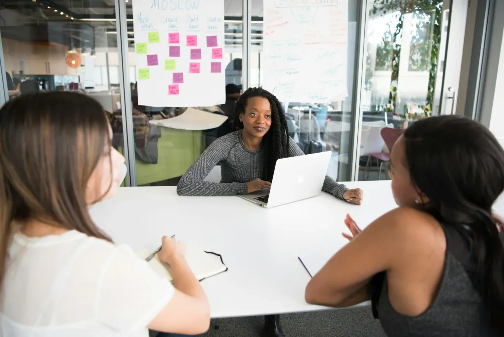 Three colleagues planning together with a laptop, notebooks and notes on a glass wall